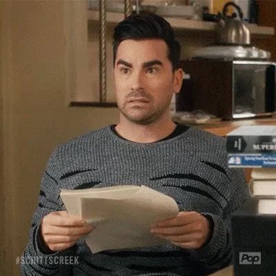 David Rose from Schitt's Creek holds a stack of papers. He has an awkward look on his face.