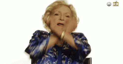 Older woman, Betty White dancing in her chair and raising her hands in excitement.