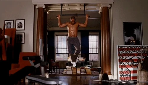 Will Smith working out in a formal room on a pullup bar attached to the door frame. 