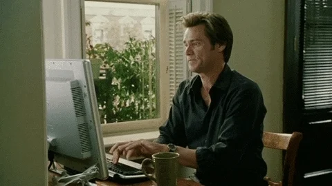 Jim Carey sitting at desk in front of computer frantically typing on keyboard.