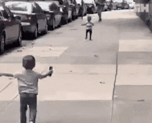 Two small children run towards each other on a sidewalk and embrace in a hug