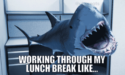 A shark at a work cubicle. It chomps at the air. The text reads, 'Working through my lunch break like...'