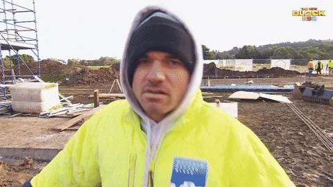 A construction worker on a building site leans forward and asks, 