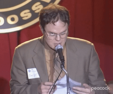 gif of man on stage in front of a microphone, holding papers and looking nervous