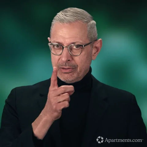 Old man with gray hair, glasses, and black clothes pointing fingers with a disapproving expression