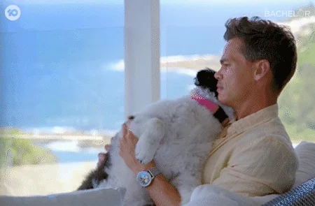 A man sitting by a window, holding his dog in his lap.