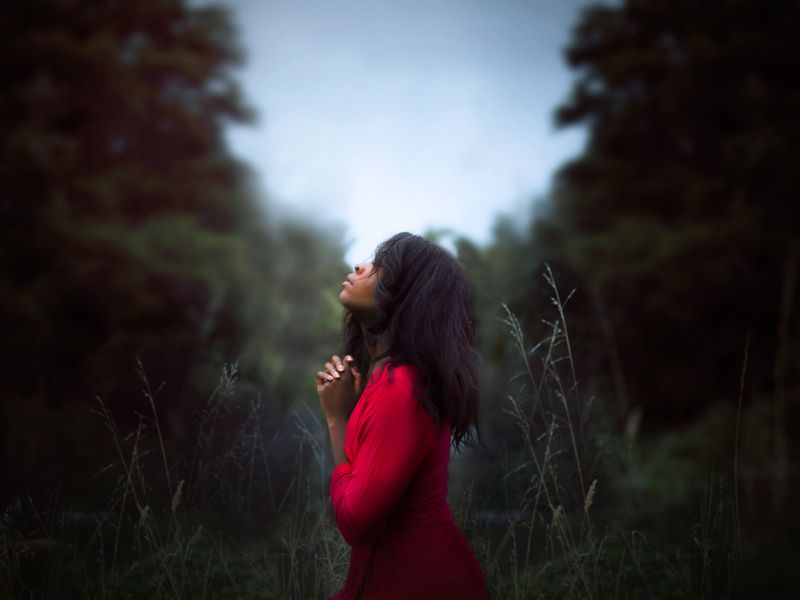 Black woman praying in nature, head held up to the sky