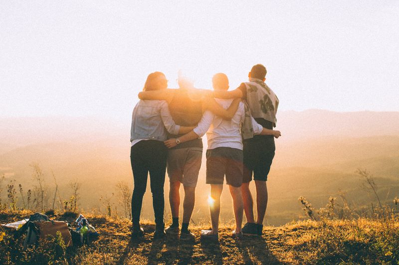 A group of people hugging each other and watching the sunrise on top of a hill.
