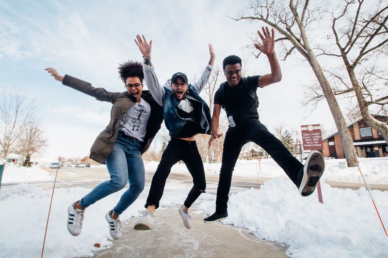 Three people are jumping in the air. They're smiling and have their hands up. There is snow on the ground around them.  