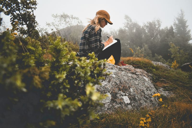 A woman sits in nature journaling. 