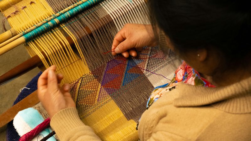 An Indigenous woman weaving a patterned fabric. 