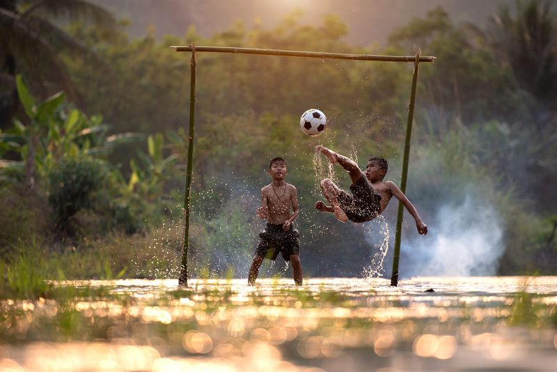 Two boys playing football in a makeshift goal made of bamboo canes.