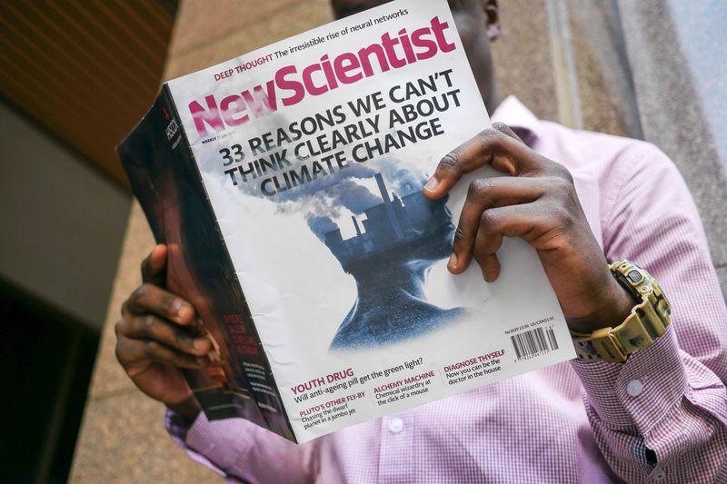 A person reading New Scientist magazine. The cover story is '33 reasons we can't think clearly about climate change.'