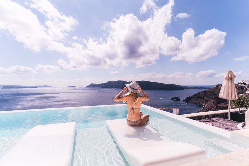 A glamorous woman sitting in an infinity pool overlooking a beautiful sea view.