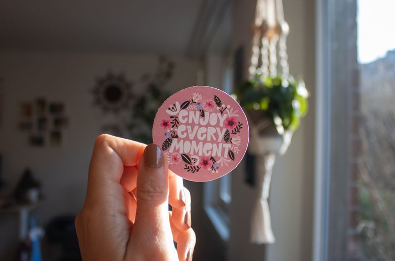 A girl is holding a circle-shaped paper that says- enjoy every moment