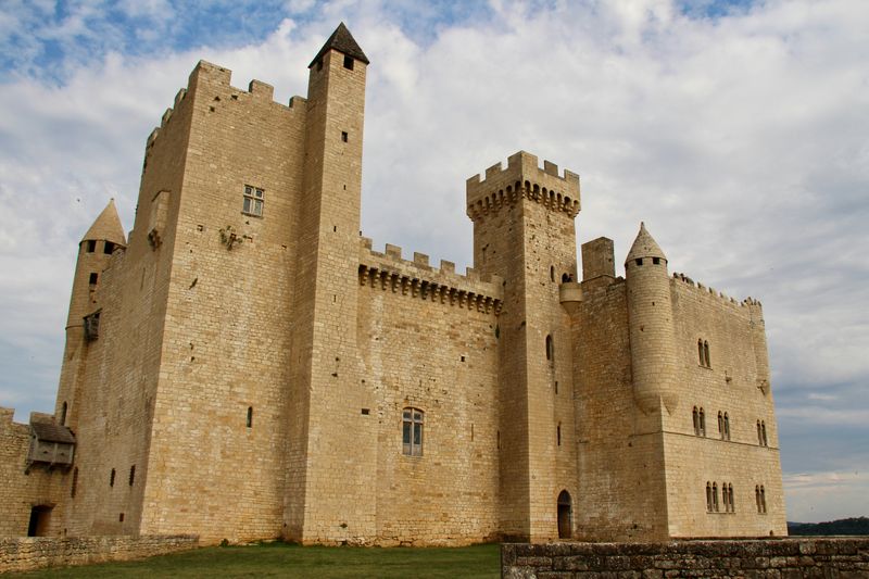 A castle made of yellowed brick with tall sections on the left and middle right and lower, boxy parts.
