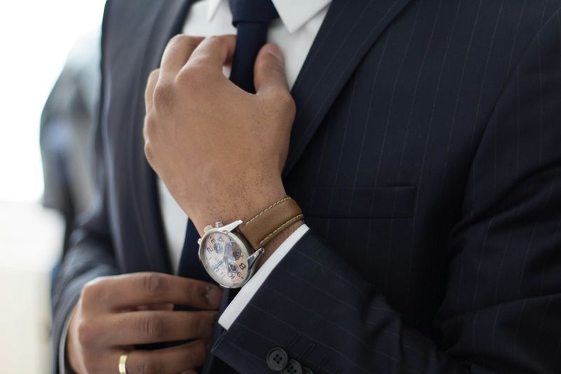 A man dressed in formal attire adjusts his tie.