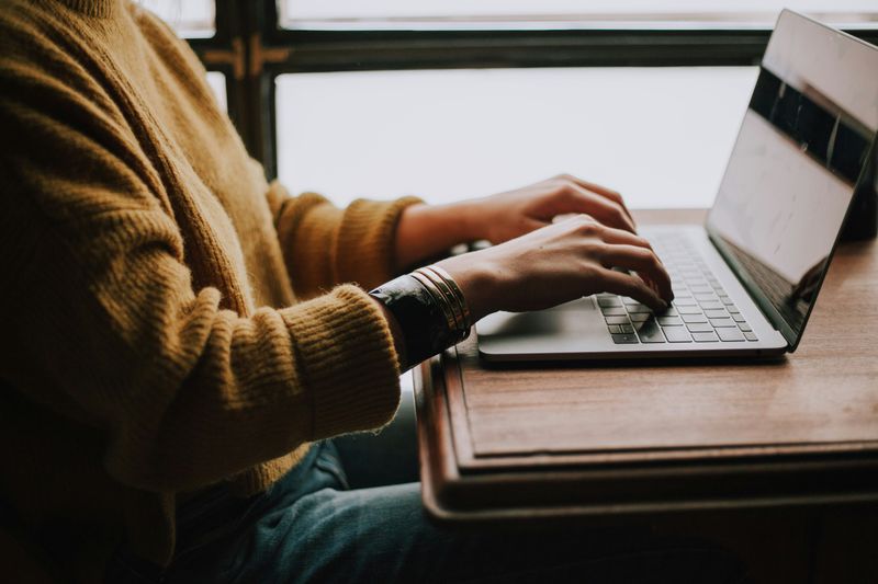A student sitting at a desk and typing on a laptop.