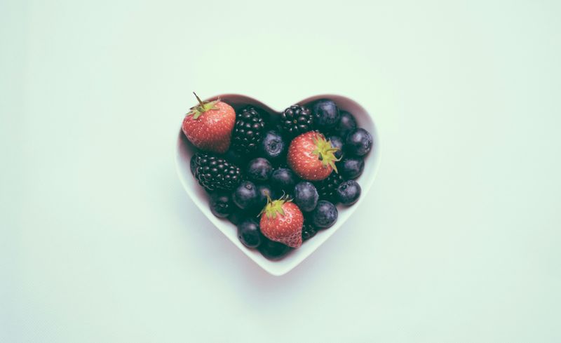 A small heart-shaped bowl is filled with fruits.