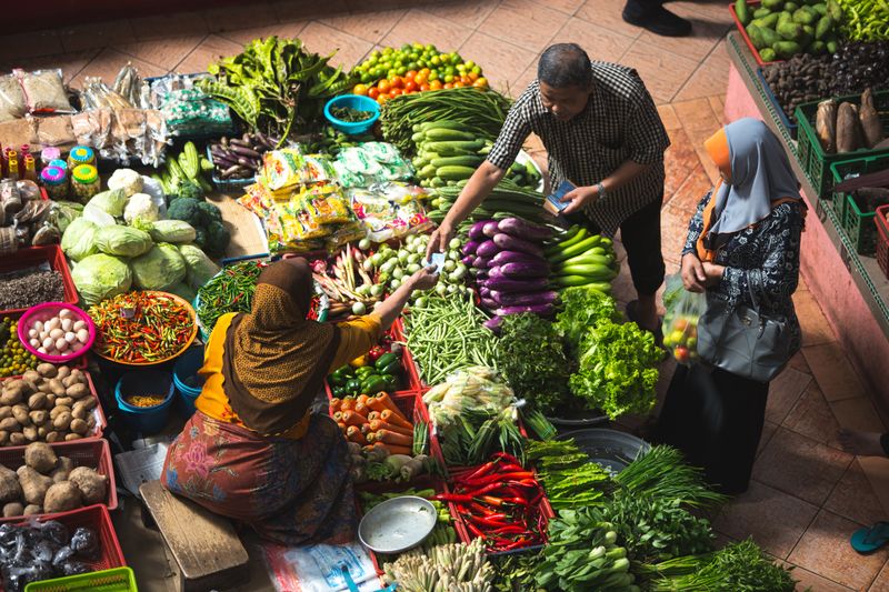 A woman is sitting around lots of fruits and vegetables. She is taking money from a man.