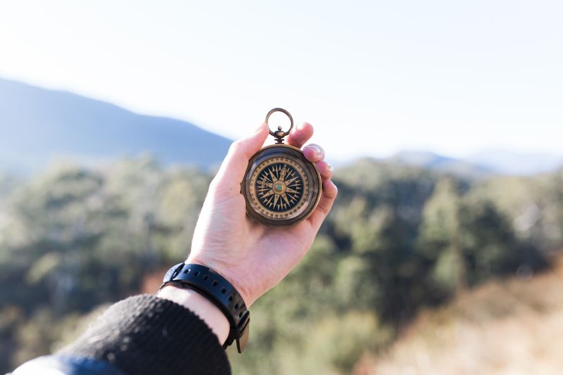 A hand holding a compass overlooking a mountain path