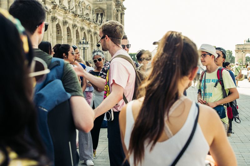 A tour guide with a headset speaking to a group in a European plaza.