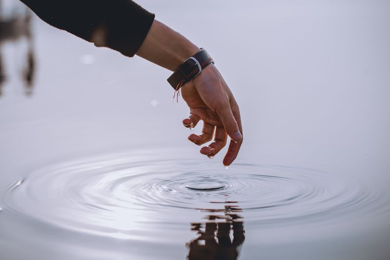 A hand dips into water, creating the ripple affect.