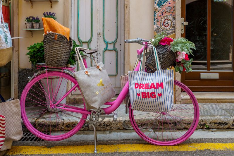 Pink bicycle at city curb loaded with baskets and bags of produce and other items.