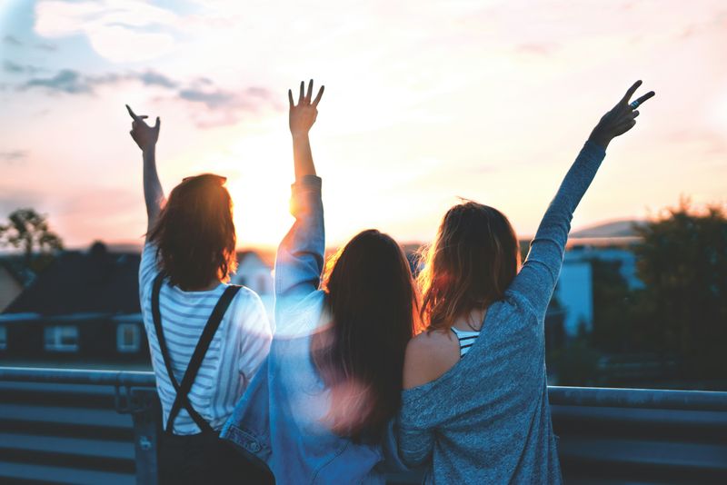 Three young people facing suburban area at sunset with their hands raised.