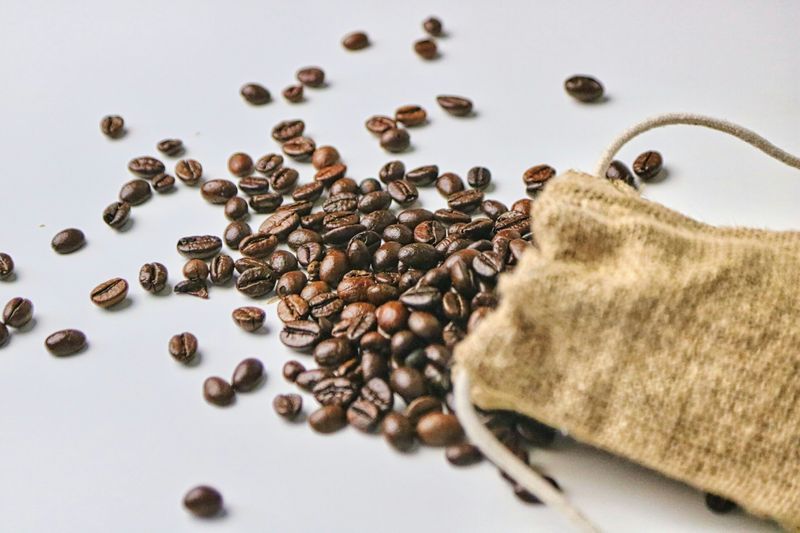 A small satchel of coffee beans spilling out on a white surface.