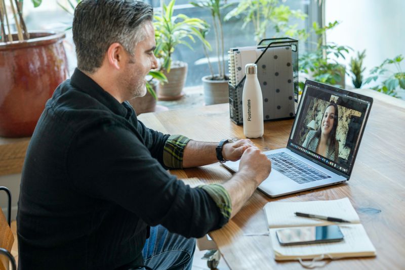 Photo of mature Caucasian male sitting at a desk in front of a laptop having a virtual meeting with a female 