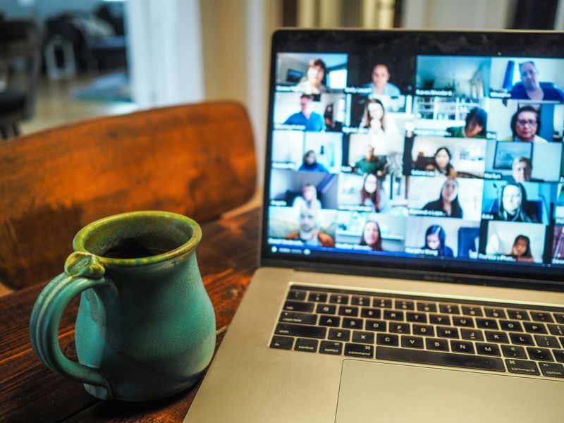 A Zoom meeting displayed on a laptop featuring a green mug set on a wooden table. 