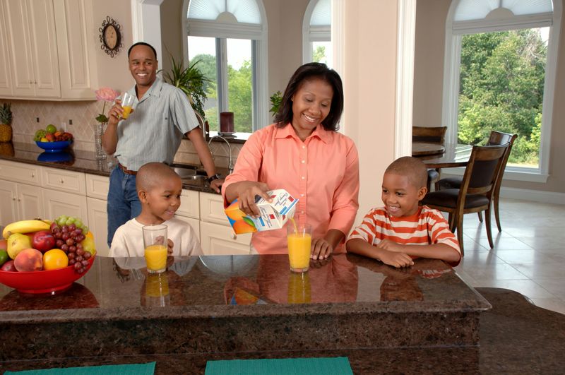 A picture of a man, woman and two boys in a kitchen enjoying a some orange juice.