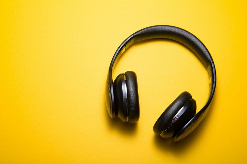 A pair of black over the ear headphones laying on top of a yellow background.