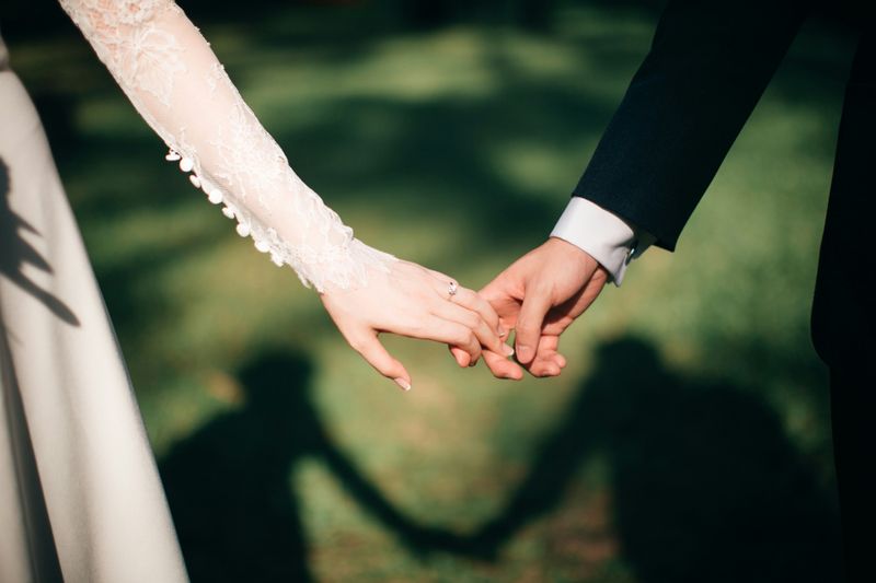 A close up photo of a bride and groom holding hands.