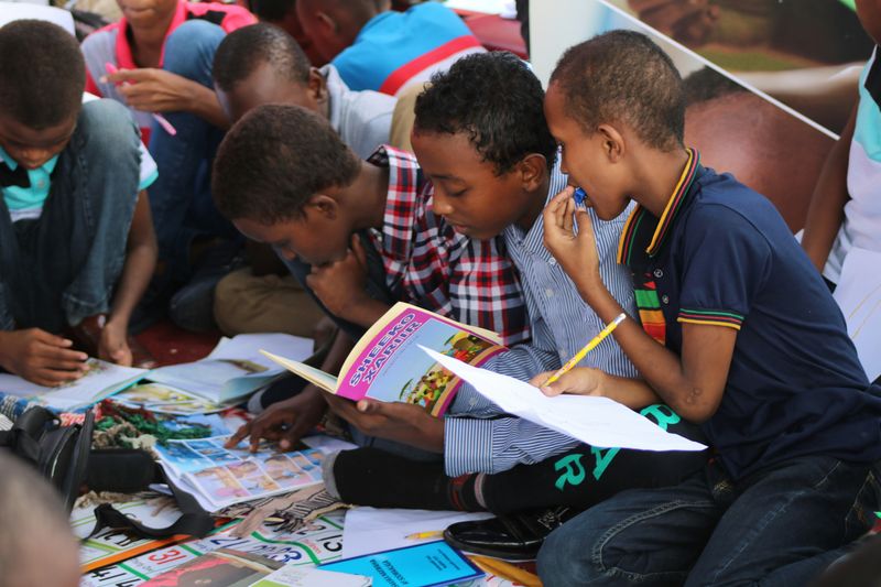 A group of students sitting on the ground learning together with different books and learning materials.