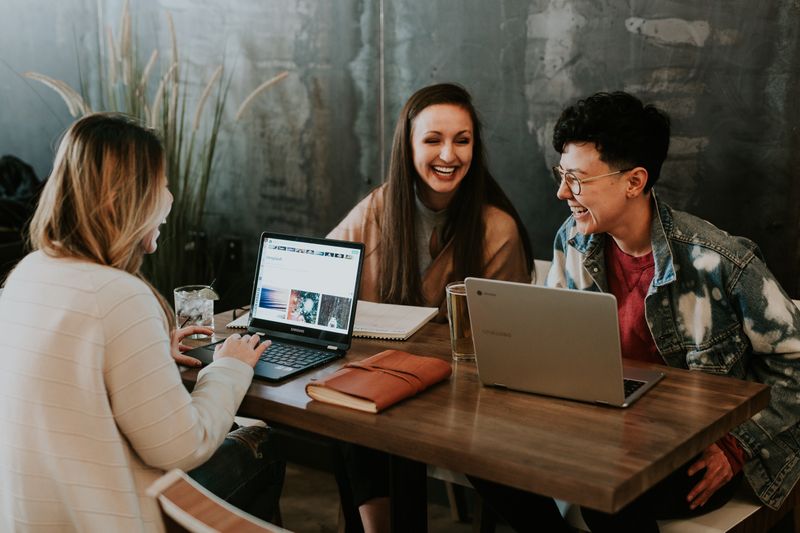 a group of cheerful people sitting at a table with laptops