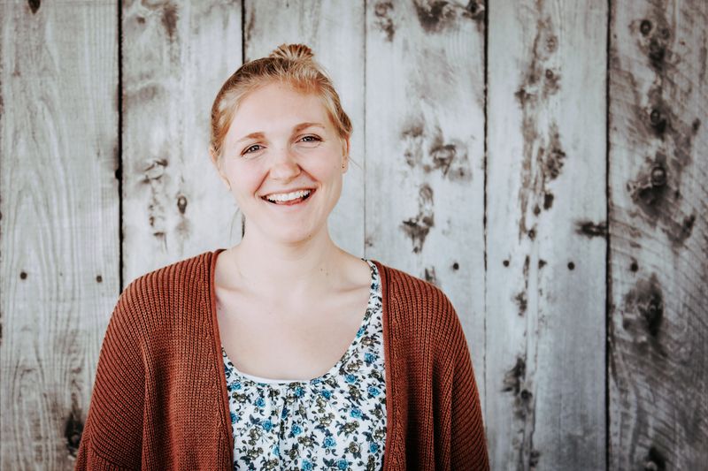 Young woman in front of gray plank wall. Hair is up and she is casually dressed