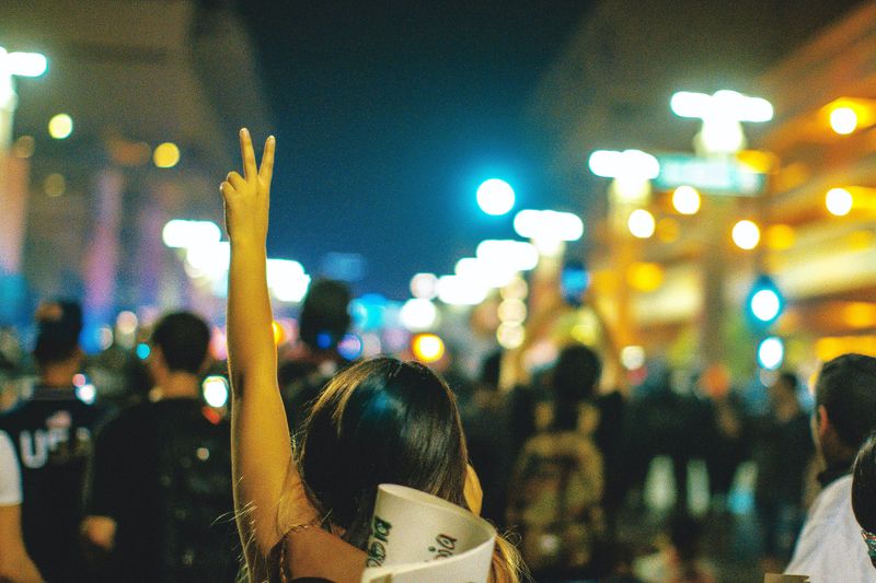 A woman at a protest holding up the peace sign with her hand.