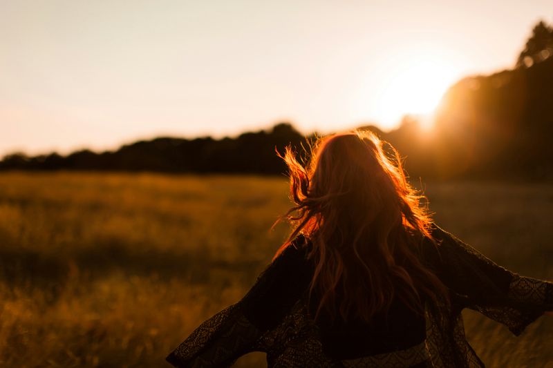 A woman feeling free with her arms open wide in a field with the sun rising in the distance