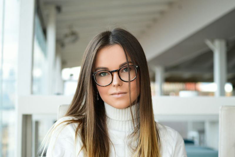 A young woman with glasses and a stylish turtleneck sweater in an office.