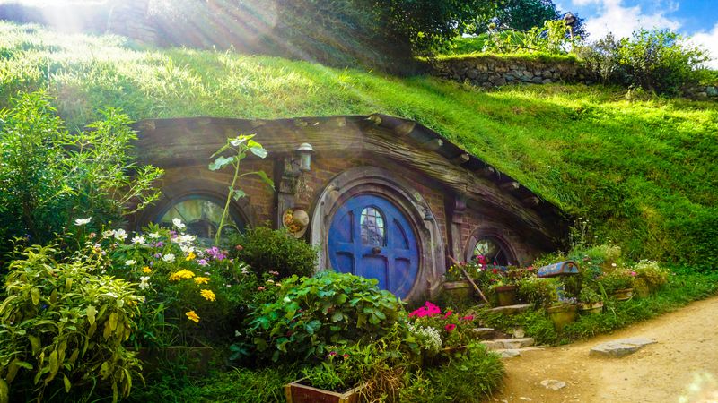 A magical looking outdoor scene with a tiny door emerging from a small hill.