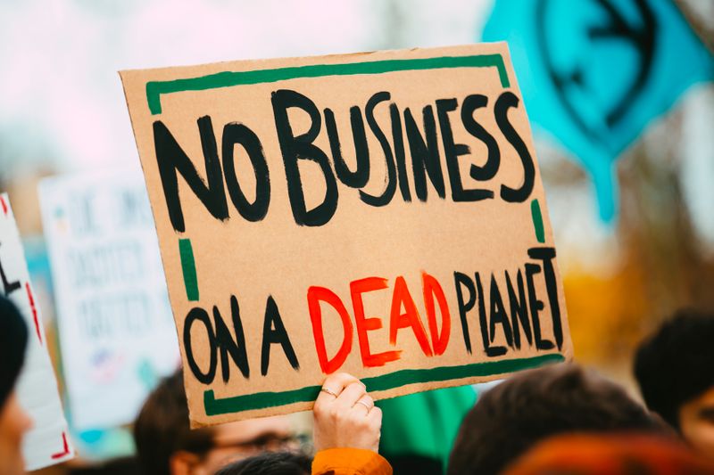 A hand holding a cardboard sign reading 'no business on a dead planet'.