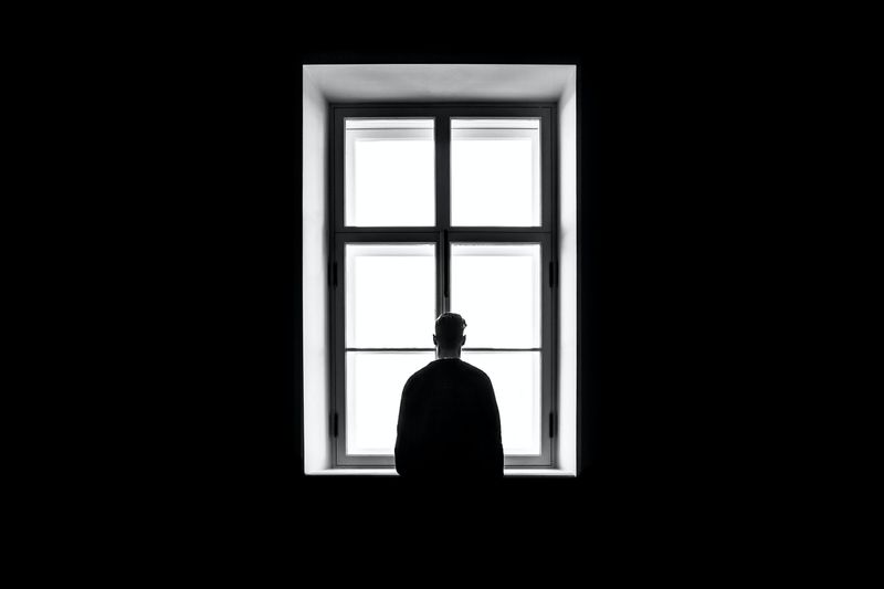 A person in a dark room looking out a large window.