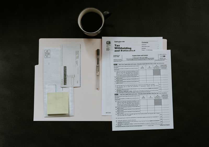 Tax documents in an open folder. A pen and cup of coffee are next to the documents.