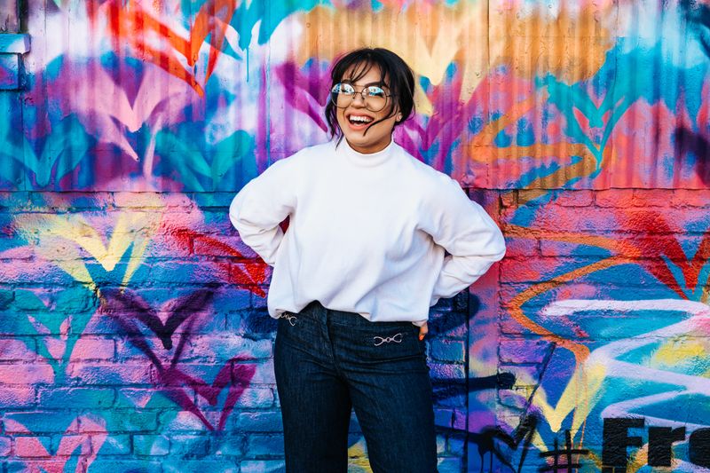 Smiling woman standing in front of a colorful brick building.