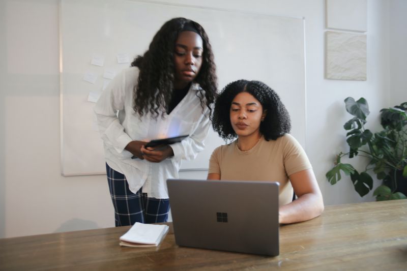 Image: Two people look at a screen to review work together in a conference room with a plant.