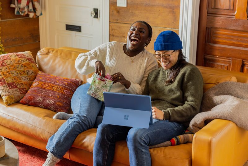 A picture of an African-American and Asian woman laughing together on a couch. 