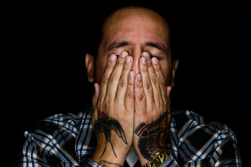 Close up of a male's face holding his two tattooed hands to his face covering his mouth, nose and partially his eyes.