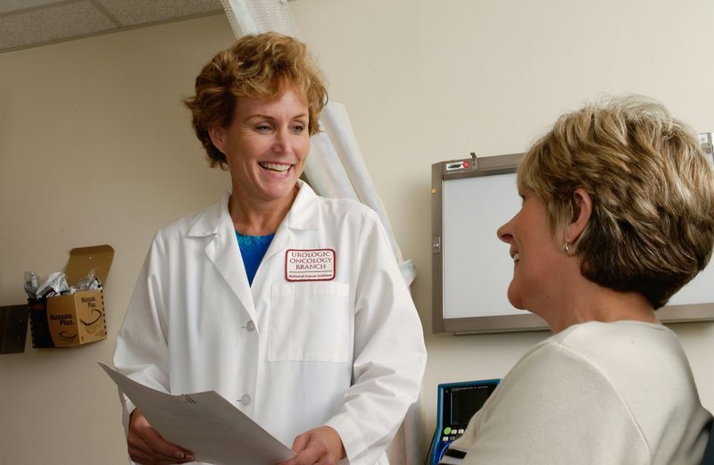 A therapist (standing) smiles at their patient (sitting).